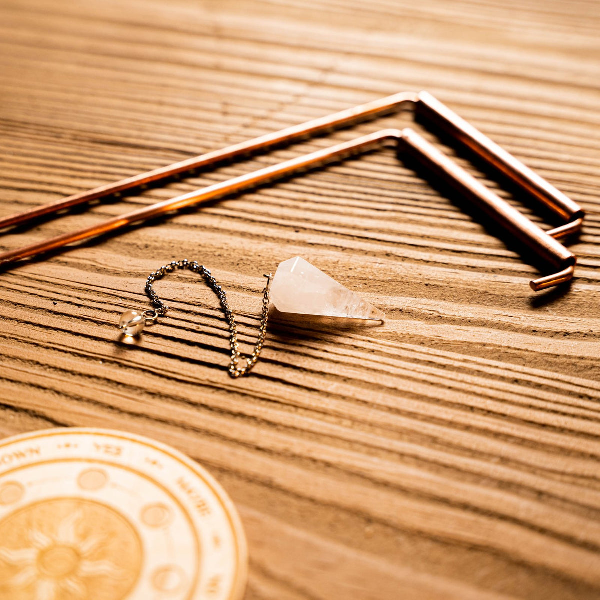 Copper dowsing rods, the quartz pendulum and the engraved wooden answer board on a wooden table.